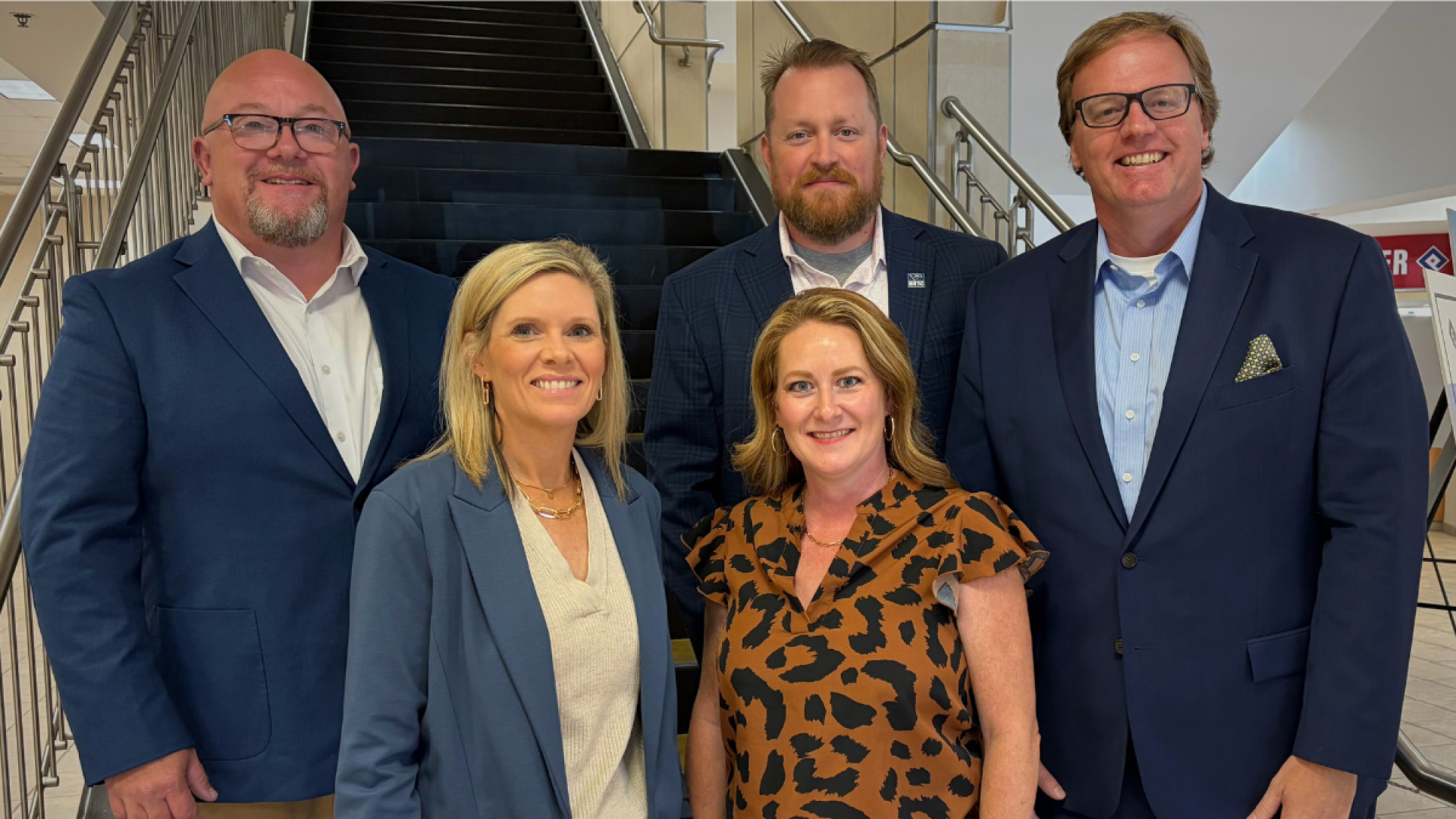 Five Black River Technical College staff members in business attire pose together in front of a staircase at the Arkansas Deans Association Annual Meeting.